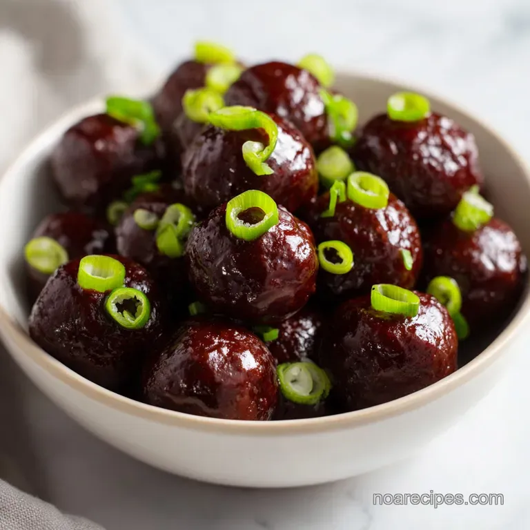 Glossy brown meatballs arranged on a white platter, drizzled with sauce and topped with bright green scallions.