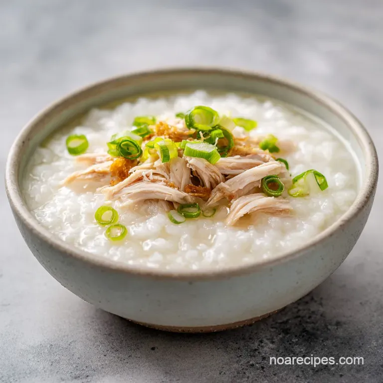 Steaming white rice porridge in a shallow bowl, paired with dark wooden chopsticks and a splash of red chili oil.